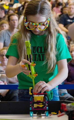Photo by John Fike. A young girl repairs a lego robot while wearing glasses made from legos.